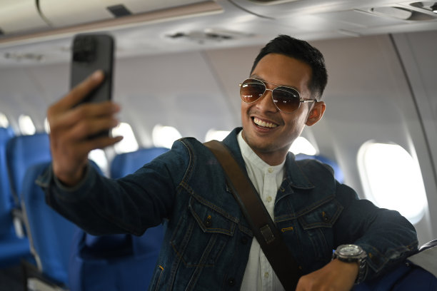 自信的亚洲男性旅行博主靠在飞机座位上，拿着相机录制他的视频博客。图片下载