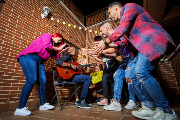 一名男子一边弹吉他，一边和他的朋友们在室外的露台上庆祝。图片下载