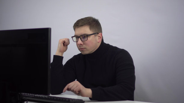 IT专家懒洋洋地在电脑上打字。一个戴眼镜的年轻人坐在办公室里，慢慢地工作着。图片下载