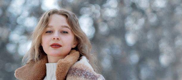 一个戴着针织帽、戴着长围巾、穿着毛皮大衣的金发女孩微笑着穿过森林。女人戴着白色手套抓雪。冬天在街上。平安夜在公园。欧洲长相的女孩享受生活。新年的心情，礼物，s图片下载