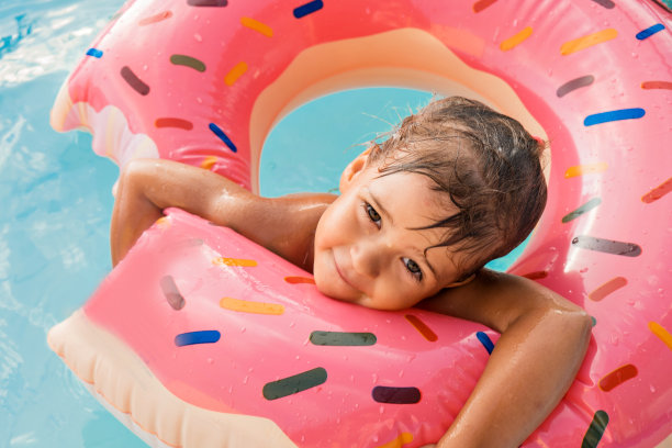 一个欧洲女孩戴着一个粉红色的大橡胶圈在蓝色的游泳池里洗澡。湿漉漉的头发和幸福的微笑。海浪、酒店和海滩。一家人正在享受一个快乐的假期。图片下载