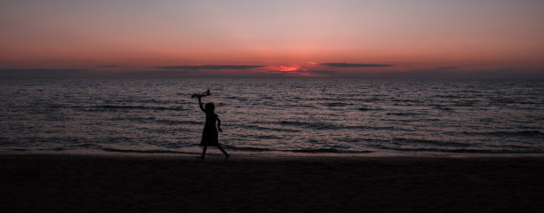 日落时分，快乐的女孩带着风筝在户外奔跑。日落时分，一个孩子在大海的背景下拿着风筝奔跑。家庭度假。图片下载