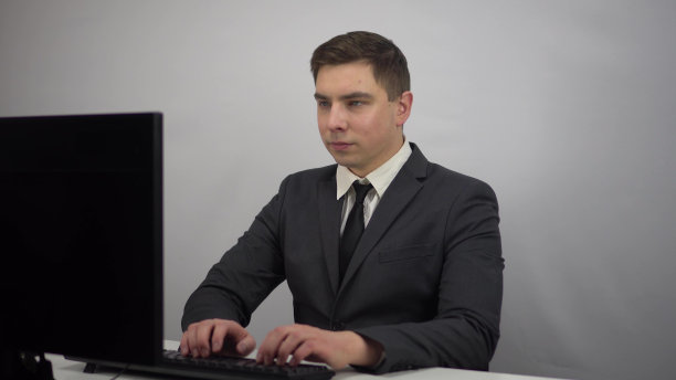 一个年轻的商人坐在办公室里，正在电脑键盘上打字。一个西装革履的男人坐在电脑前。图片下载