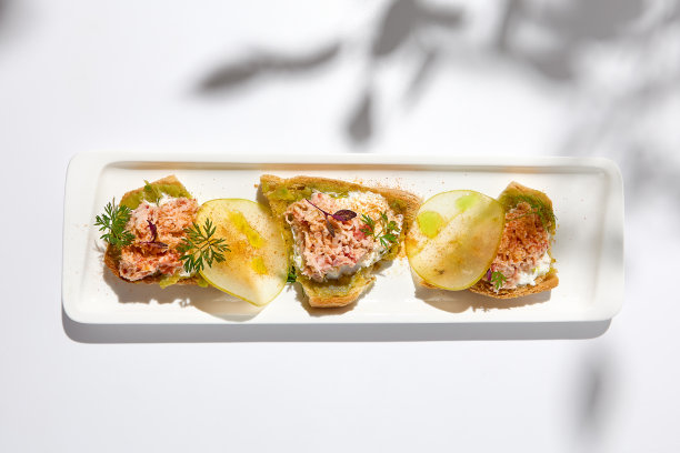 螃蟹意式烤面包的美学构图，白色背景与花朵的阴影。意大利意式烤面包配螃蟹、鳄梨和奶酪。优雅的菜单概念。图片下载