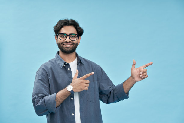 快乐的年轻阿拉伯男子指着蓝色背景上的商业广告图片下载