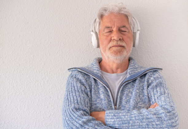 年长的大胡子男子闭着眼睛在白色背景上听音乐，戴着耳机。白发老人抱臂享受音乐图片下载