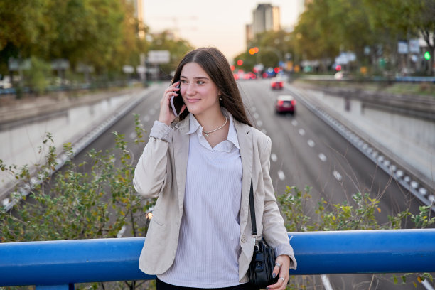 一位时尚的年轻女商人站在路边，在日落时分的城市街道上使用智能手机。图片下载