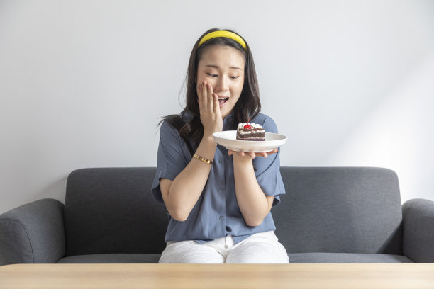 有吸引力的美丽的亚洲年轻女子的肖像抱着一块巧克力蛋糕坐在沙发上。图片下载