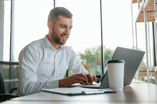 使用笔记本电脑。一个穿着正装的男人在现代化的办公室里工作图片下载