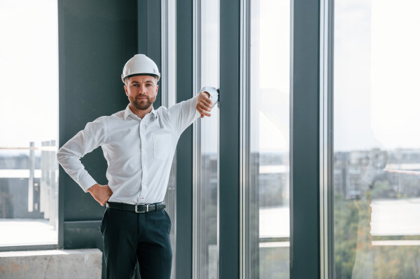 站在全景窗附近。穿白衬衫的男子正在建筑工地的室内工作。项目管理图片下载