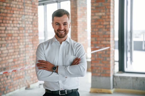 双手交叉站着。穿白衬衫的男子正在建筑工地的室内工作。项目管理图片下载