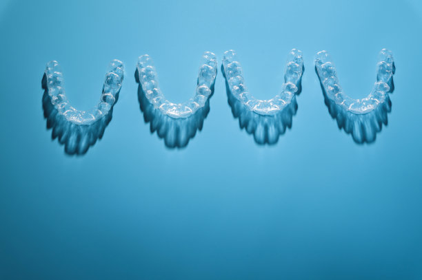 牙科诊所或正畸学背景。蓝色背景上，一排看不见的塑料新牙套，工作室用阴影拍摄图片下载