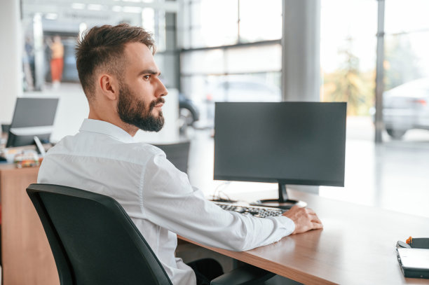 坐在桌旁。一个穿白衣服的年轻人在汽车经销店里图片下载