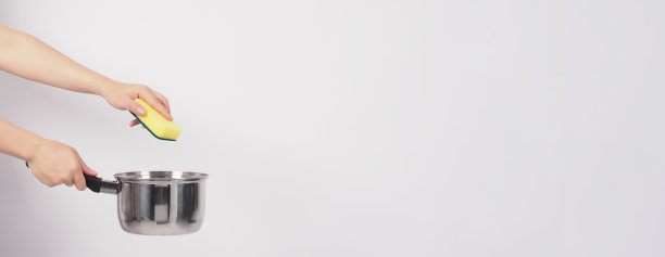 清洁锅的人在白色的背景上用方便的洗碗海绵清洁不粘锅，软的一面是黄色，硬的一面是绿色，以保证烹饪后的卫生。电锅图片下载