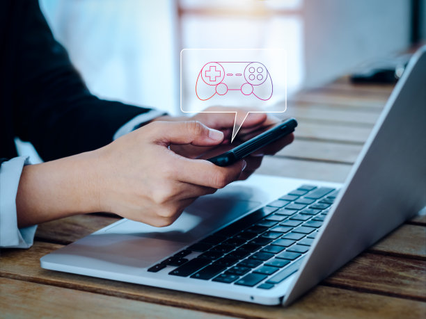 游戏控制器，气泡语音符号中的操纵杆图标出现在商人手中的智能手机上，水平，同时工作的笔记本电脑。手机游戏、智能手机游戏模式概念。图片下载