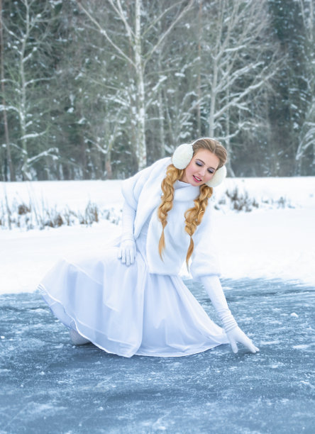 冬天穿着白衣服的女孩在冰上溜冰。在冰湖上骑行，背景是白雪覆盖的森林图片下载