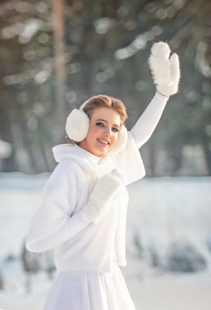 在一个阳光明媚的冬日，一个可爱的金发少年，穿着白色皮大衣，戴着白色的棉球帽和白色的连指手套，在户外端着一个冒着热气的透明玻璃杯子，里面装着冰块。挥舞的手图片下载