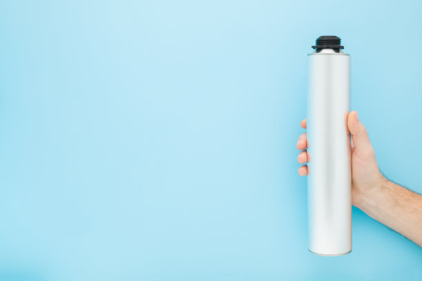 年轻的成年男子手拿浅灰色金属容器的专业泡沫喷枪在浅蓝色的墙壁背景。柔和的颜色。特写镜头。侧视图。文本的空白位置。图片下载