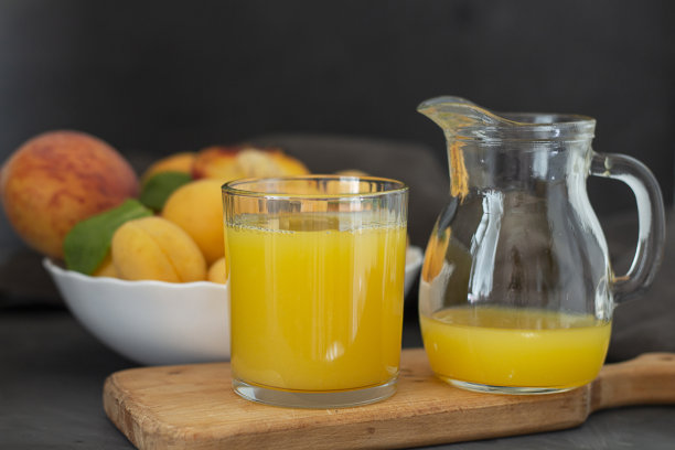 新鲜果汁。杏子和桃子。新鲜健康的果汁在一个玻璃杯和玻璃瓶在厨房板上。本空间图片下载