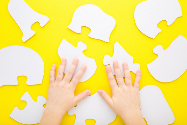 宝宝双手准备开始放拼图。在明亮的黄色桌子背景上，白色拼图大形状。特写镜头。视角镜头。游戏开始。孩子的发展。自顶向下视图。图片下载