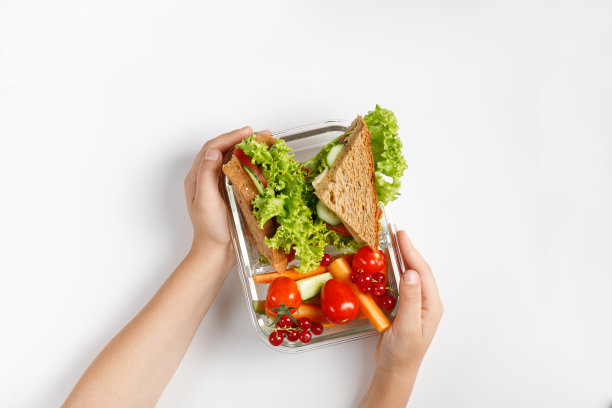 小孩子的餐，拿走学校的餐。学校午餐装在盒子、容器里。吐司，三明治，蔬菜点心。孩子的手。图片下载