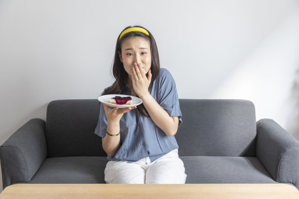 年轻中国女人在家吃芝士蛋糕，幸福微笑图片下载