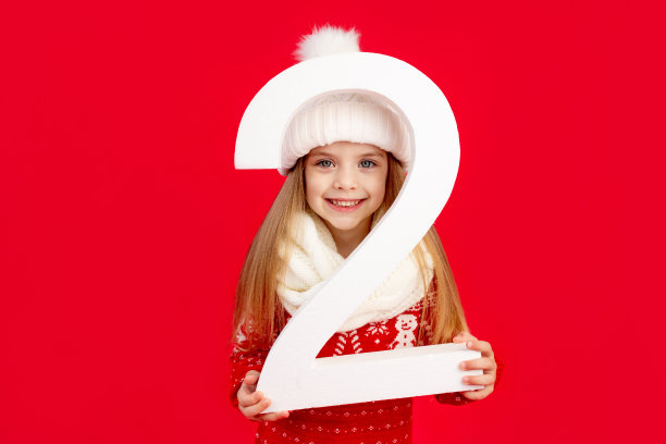 一个小女孩戴着冬天的帽子和毛衣，红色单色孤立的背景上有一个很大的数字2，她高兴地笑着，新年和圣诞节的概念，文字的空间图片下载