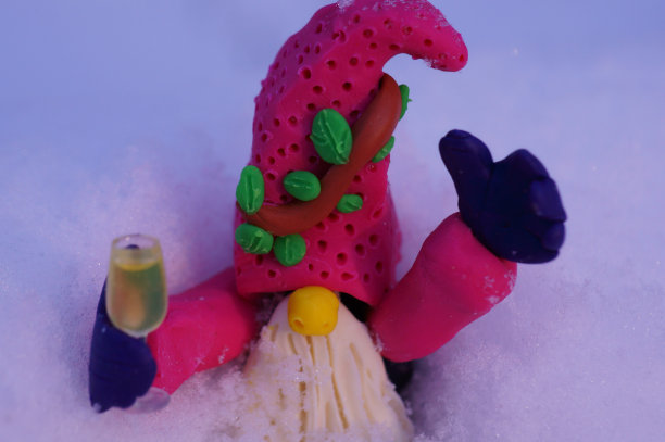 一个用橡皮泥做成的小矮人，手里拿着一杯香槟，背景是白雪。图片下载