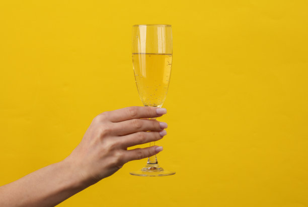 女人的手拿着黄色背景的香槟酒杯。有创意的想法。”图片下载