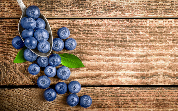 成熟的蓝莓放在一张木桌上，盛在一个金属勺子里图片下载