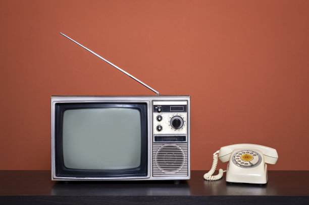 复古的老式电视接收器和老式的电话在客厅的木桌子上，橙色的墙壁背景图片下载