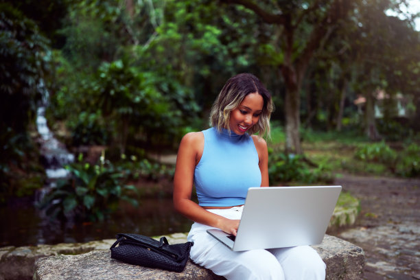 一名年轻的巴西女子微笑着拿着笔记本电脑坐在户外公园，在里约热内卢里约热内卢图片下载