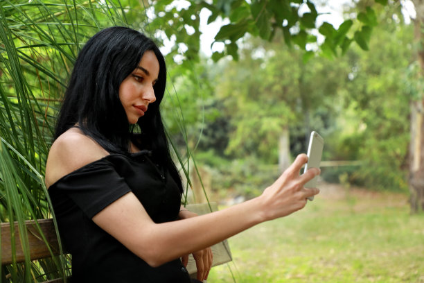 美丽的年轻女子坐在户外公园的长椅上使用智能手机图片下载