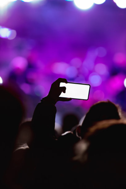 手持智能手机的人和舞台灯光下音乐会人群的剪影图片下载