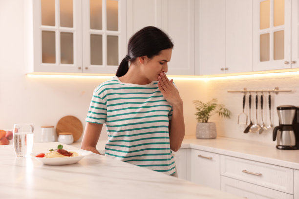 年轻女子在厨房看到餐桌上的食物时感到恶心图片下载