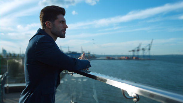 自信的商人在早晨的阳光下在海港起重机的阳台休息图片下载