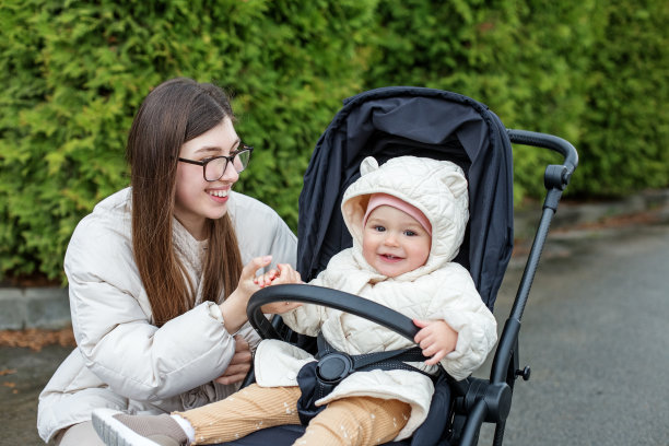年轻的母亲抱着婴儿走在漂亮的黑色婴儿车里。凉爽的天气。幸福的家庭图片下载