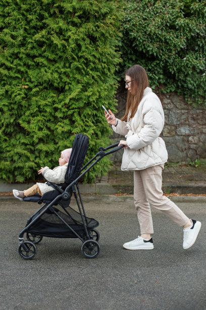 年轻的母亲抱着婴儿走在漂亮的黑色婴儿车里。凉爽的天气。幸福的家庭图片下载