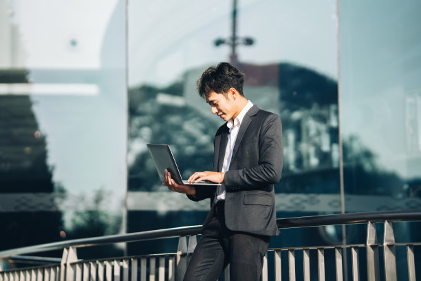 年轻英俊的经理坐在户外的楼梯上，用笔记本电脑工作，工作生活平衡的概念。图片下载