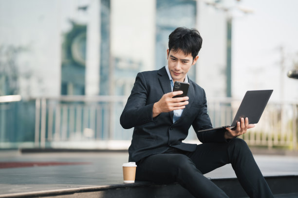 年轻英俊的经理坐在户外的楼梯上，用笔记本电脑工作，工作生活平衡的概念。图片下载