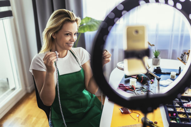 年轻女子配饰设计师在工作室车间制作手工珠宝并录制视频。时尚，创意，手工概念。图片下载