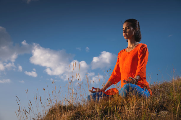 夕阳下，一名年轻的白人女子在悬崖边的草丛中冥想图片下载