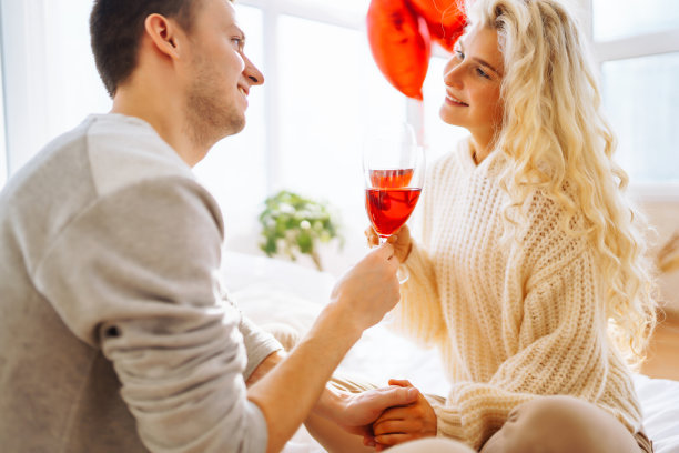 年轻情侣在家里喝红酒庆祝情人节。图片下载