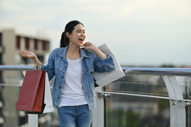 欢快的亚洲妇女携带购物袋站在阳台上的肖像。图片下载