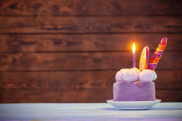 紫色生日蛋糕与燃烧的蜡烛在黑暗的木制背景图片下载