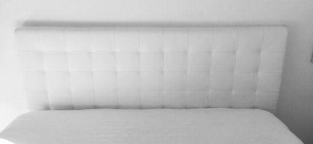 柔软的床头板。用真皮或人造革和绗缝织物制成的家具内饰。柔软的床头板靠在轻墙上。黑白单色照片图片下载