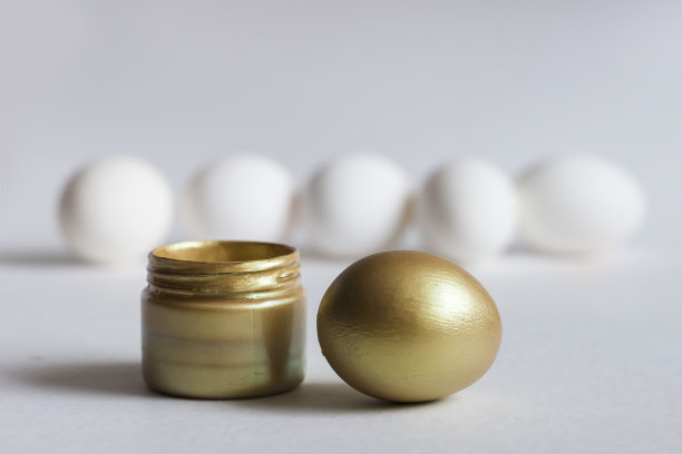 一个金蛋和一罐白色背景的金色颜料。后面有几个白色的蛋。图片下载