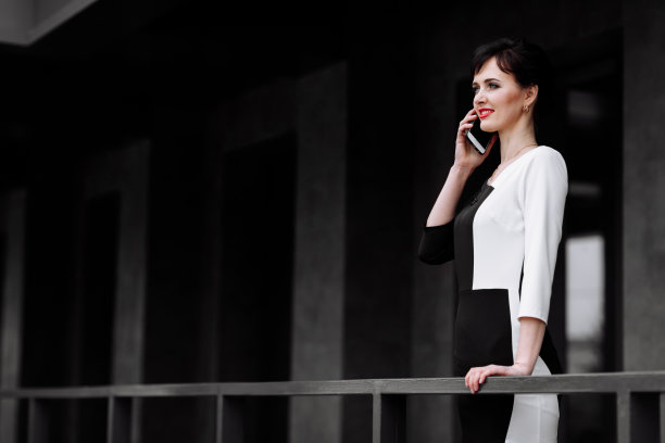 快乐的律师、女商人、职业人士正在户外用智能手机聊天。白人成功女性微笑着穿着时髦的黑白连衣裙和黑色包图片下载