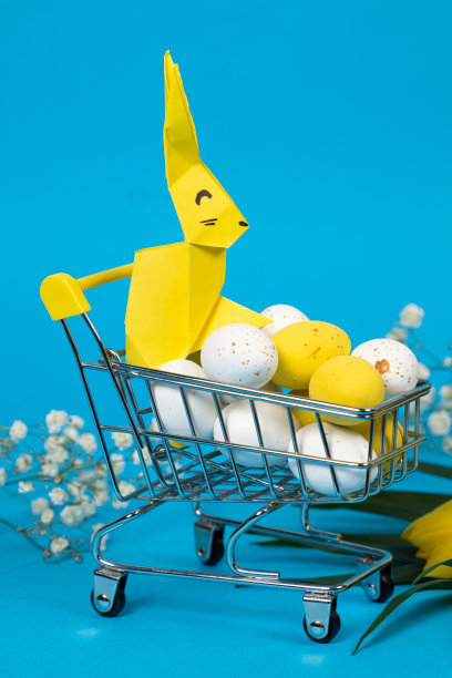 复活节白色和黄色鹌鹑画蛋和兔子在购物车上的蓝色背景。复活节大甩卖和购物图片下载