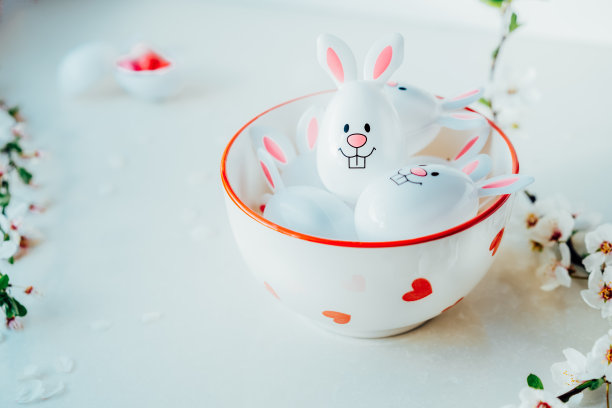 有趣的复活节彩蛋容器，里面有兔子耳朵，装满了糖果和巧克力，放在白色的厨房桌子上，上面有盛开的树枝。春节复活节作文。有选择性的重点图片下载